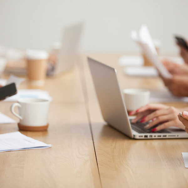 Business people sitting together at conference table office desk using laptops and smartphones working with documents, corporate project team meeting or coworking teamwork concept, close up view