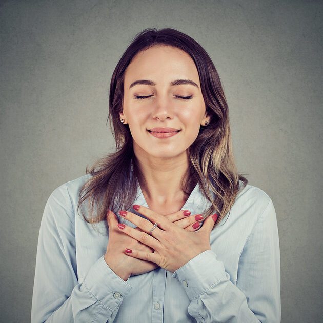 Woman with eyes closed keeps hands on chest near heart, shows kindness, expresses sincere emotions, being kind hearted. Body language feelings concept